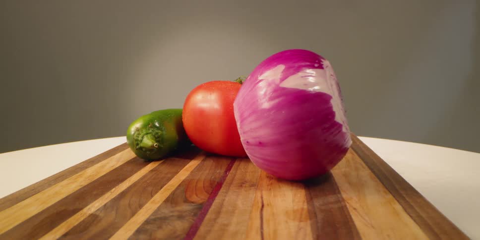 Zucchini tomato and onion sit on a wooden cutting board