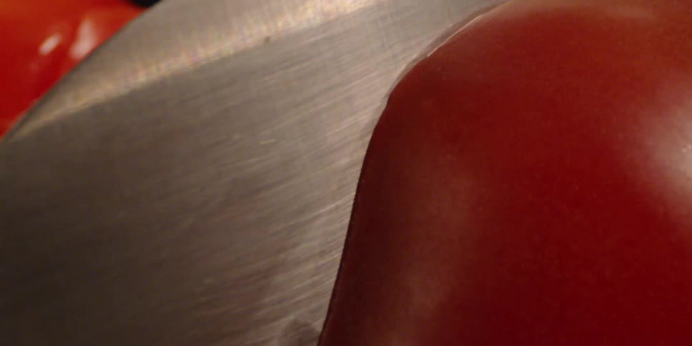A knife cuts through a tomato