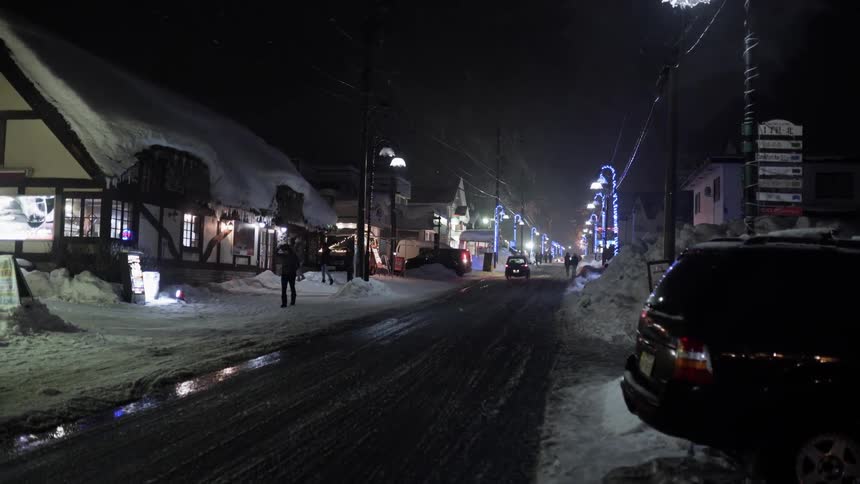 Cars and people travel on the snow covered road at night