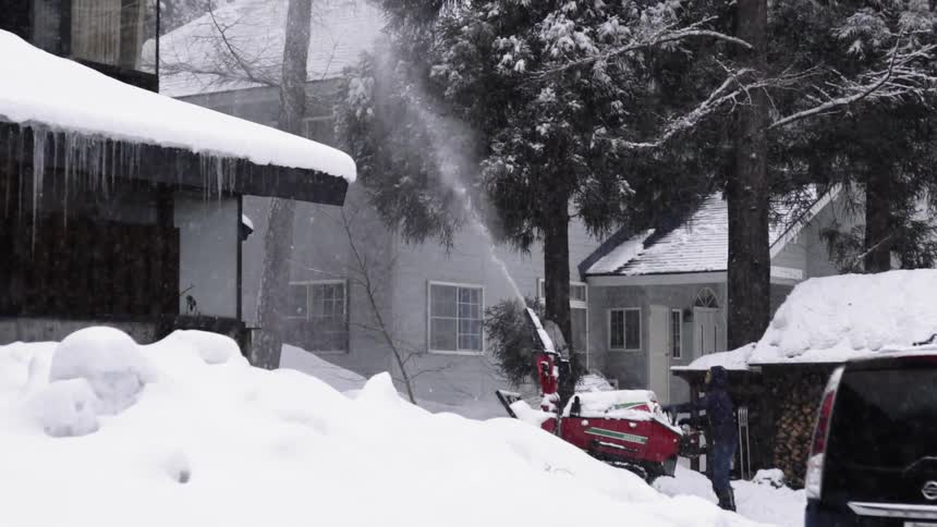 Person snow blowing a driveway in a neighborhood