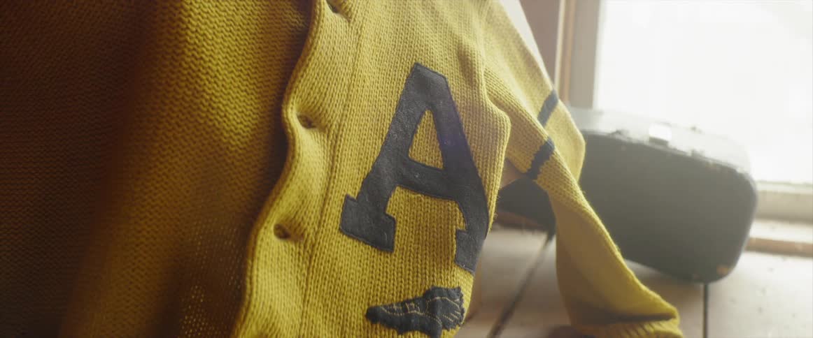 A yellow school sweater with the letter a hangs near a window
