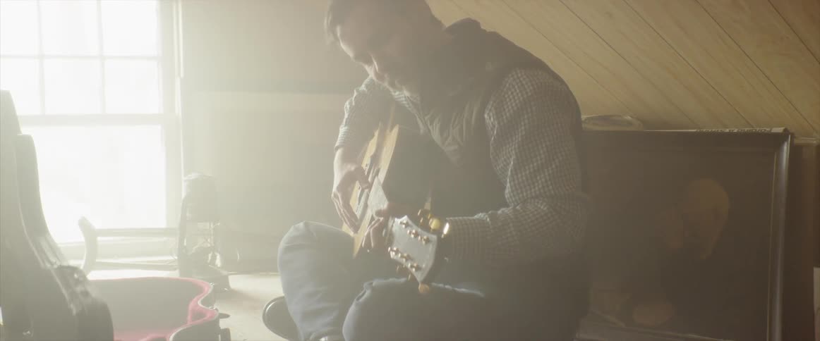 Man plays a guitar as the sun streams in the window