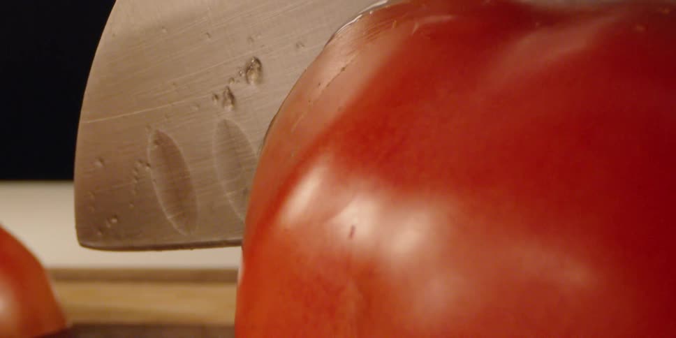 Sharp knife is slicing through a juicy red tomato