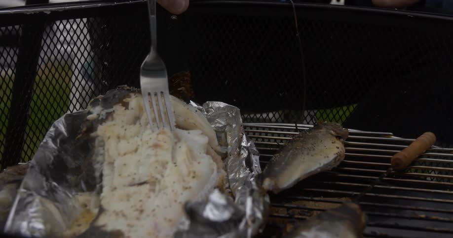 Someone flaking fish with a fork over a grill