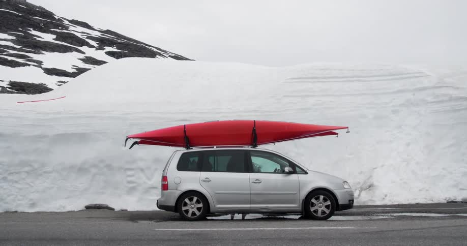 A man entering a minivan that has a red canoe strapped to the top of it during the winter