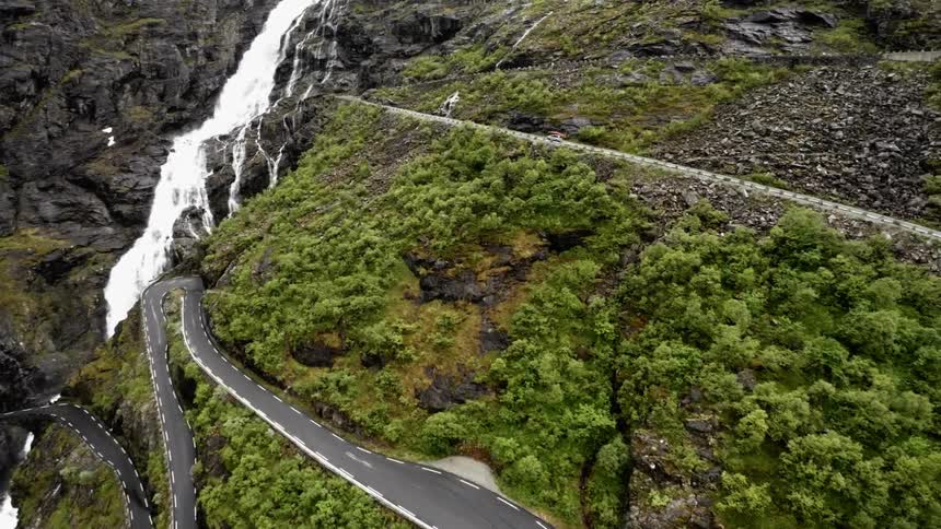 A vehicle drives on a mountain road next to a waterfall
