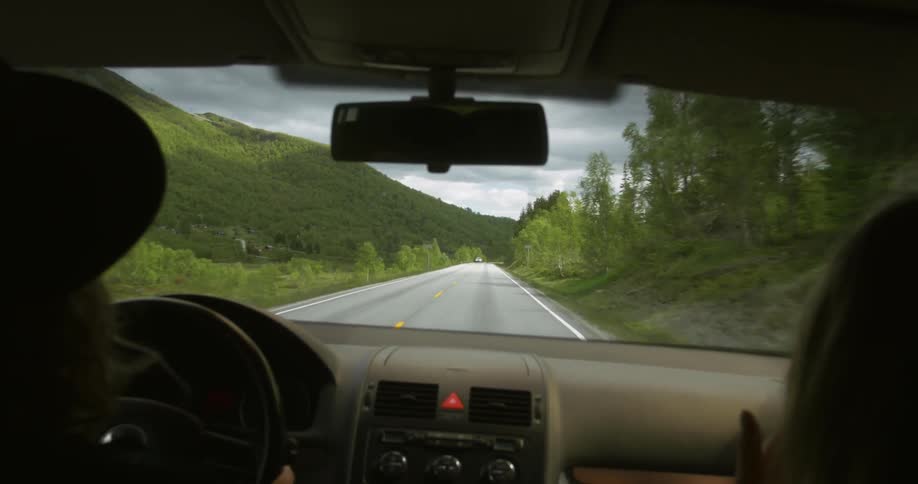 Person driving on a remote highway between plenty of greenery