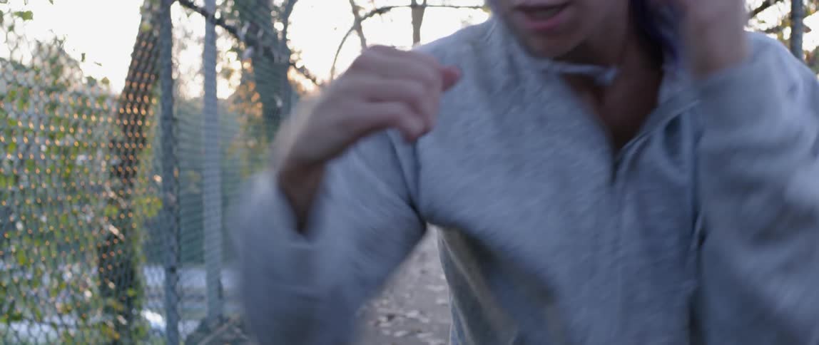 A woman wearing a hoodie shadow boxes on a pedestrian bridge over a highway