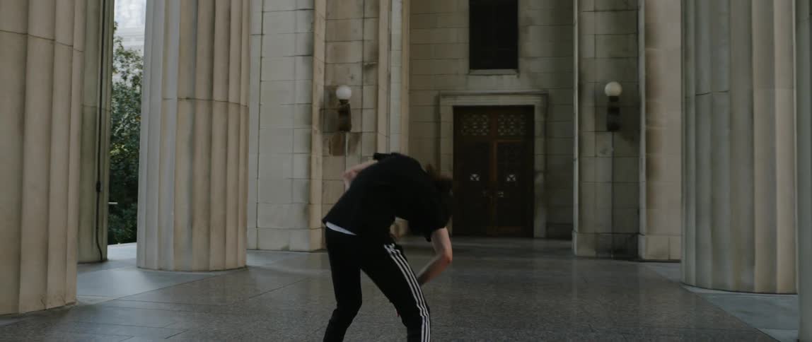 A man dances next to large building pillars