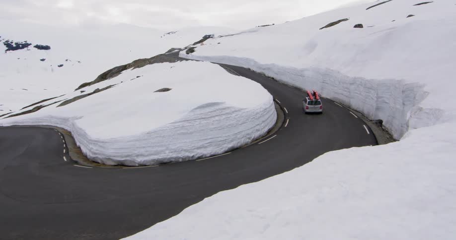 A car with red kayaks strapped to the roof driving on a winding mountain road during the winter