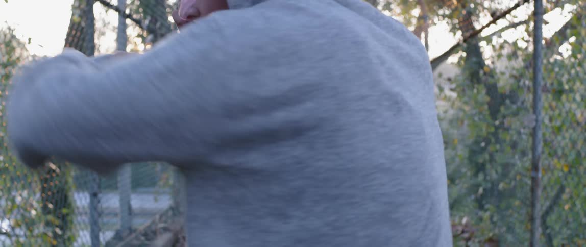 A man is shadow boxing outside by the fence