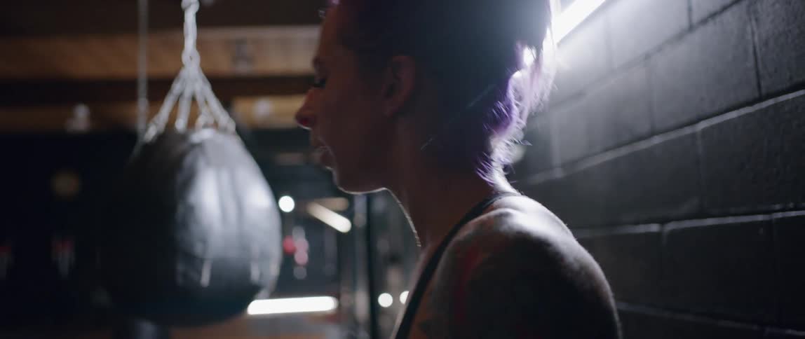 A woman breathes heavily next to a punching bag