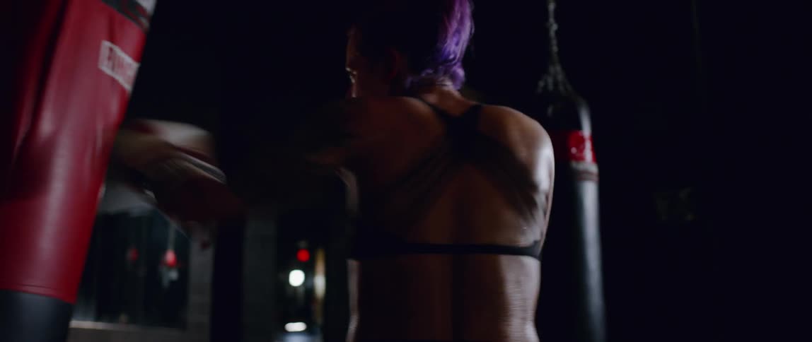 A woman with pink hair hits a heavy bag
