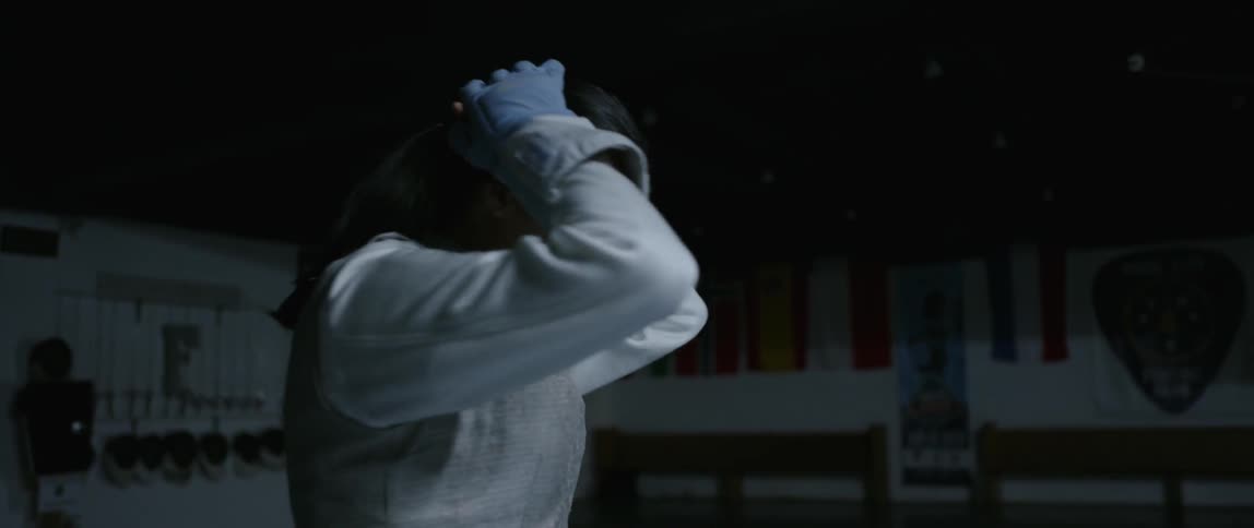 A woman in fencing gear smooths her hair