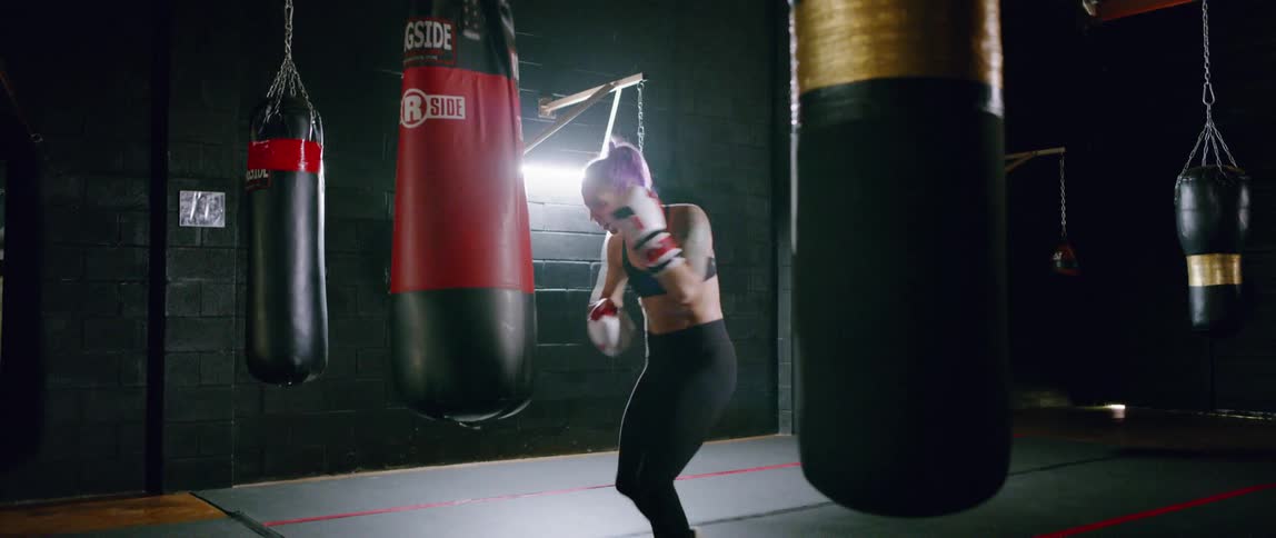 A woman is boxing a heavy bag in the gym