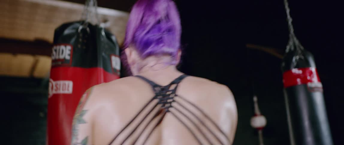 A woman with pink hair hits a heavy bag