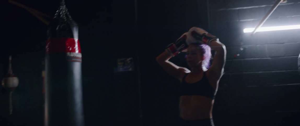 A woman wearing boxing gloves paces as she catches her breath