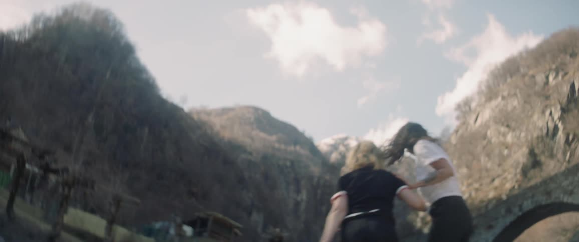 Two women climb up some rocks by a mountain
