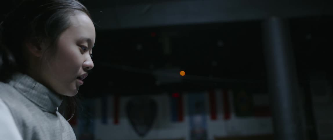 Asian woman wearing a uniform stands in a dim room