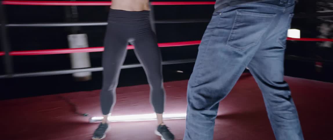Woman practices punching a man's hands in a boxing ring