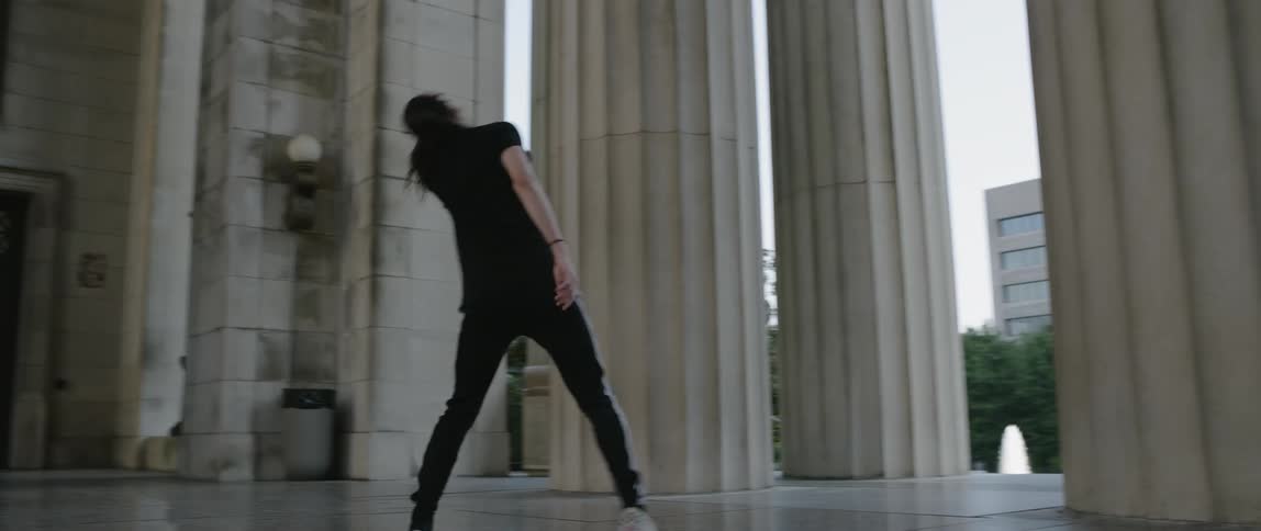 Person dances near pillars of a large building