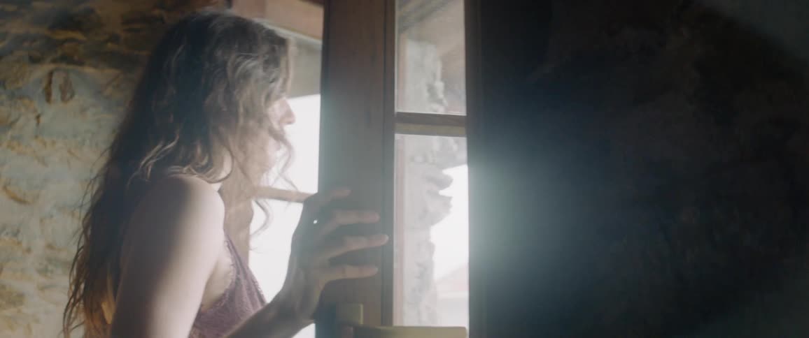 A woman is opening windows in a room and smiling during the day