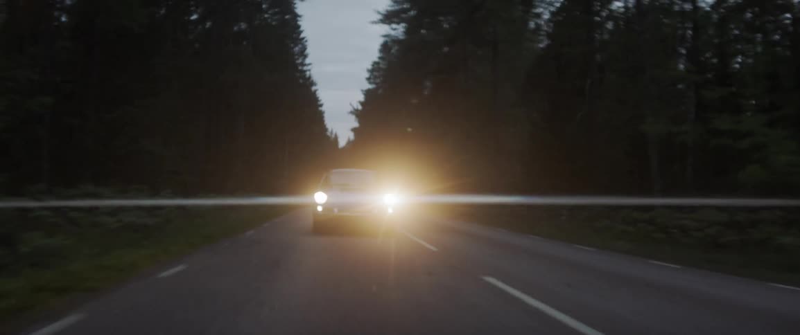 Headlights shine from a car driving down the road in the evening