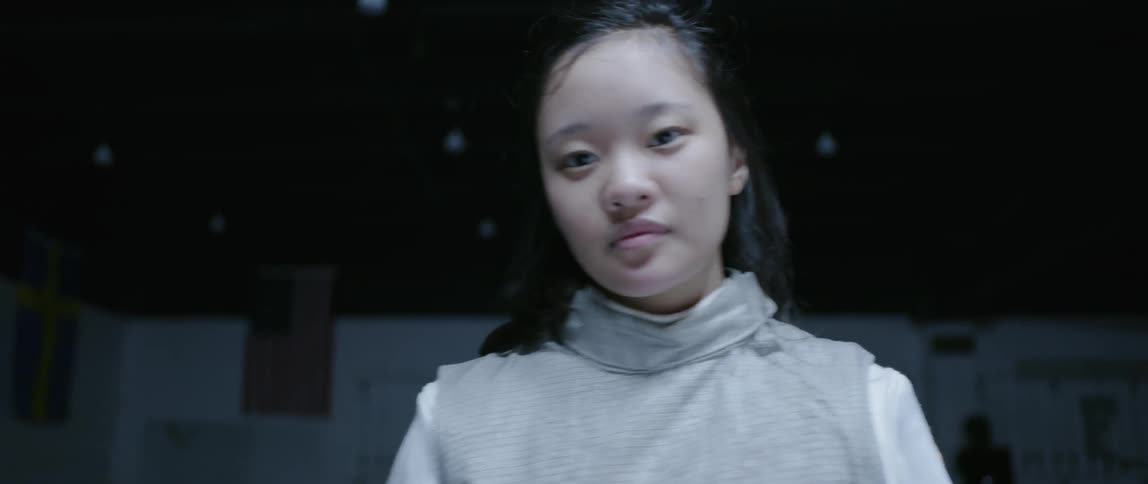 Woman removes fencing mask and gazes forward