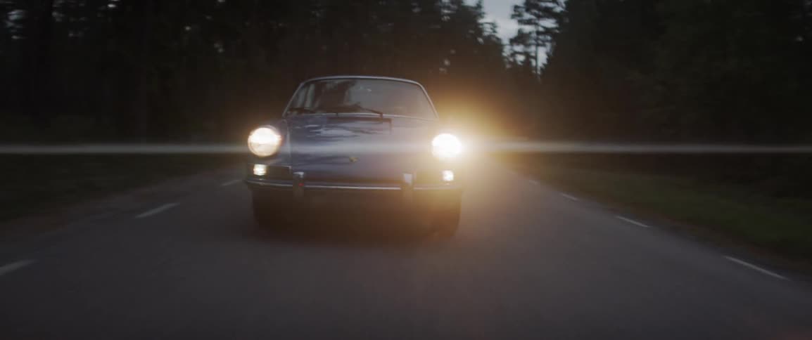 An old sports car drives on the rural road at night