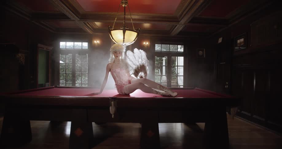 Woman poses sitting on a table waving a fan made of feathers