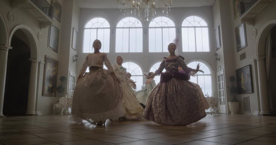 Women in ball gowns dance under a chandelier