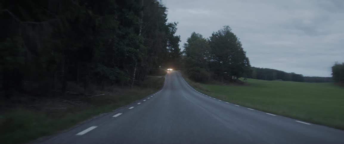 A car drives down the rural road with headlights on