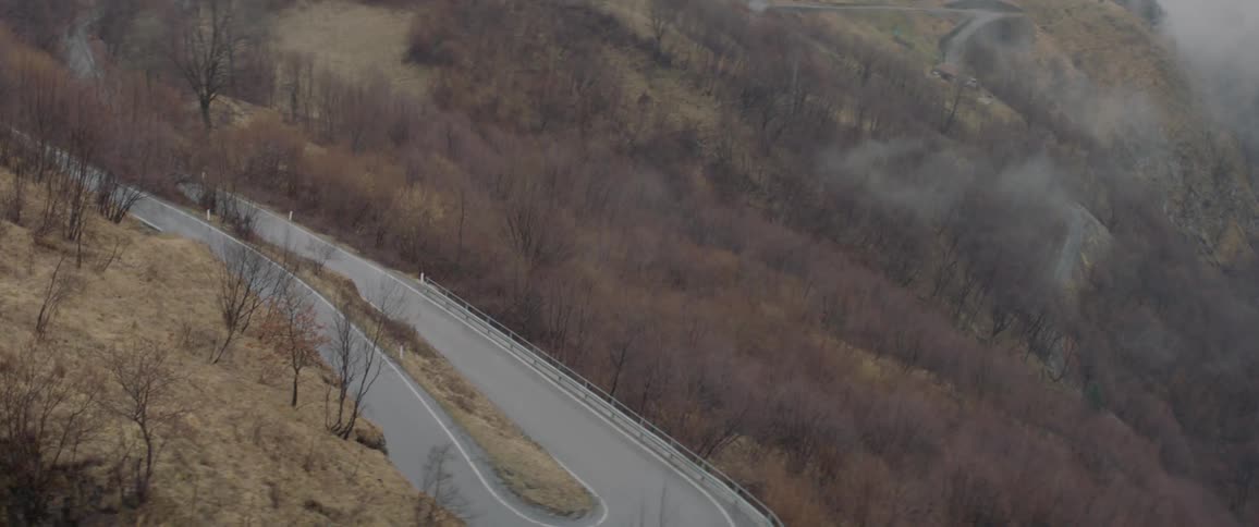 The car drives around the winding road in the rain