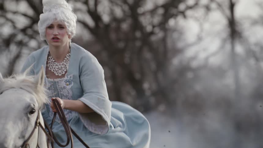 Woman wearing a white wig and dress rides a horse in a foggy field