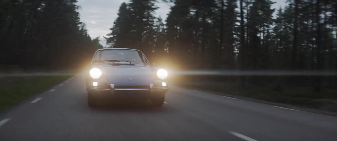 Lights shine from a car going down a road at sunset