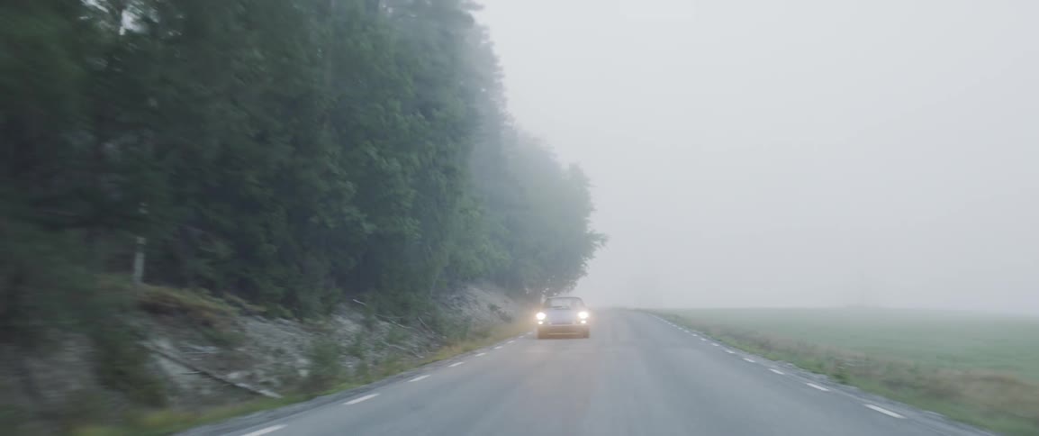 Car drives down a country road on a foggy day