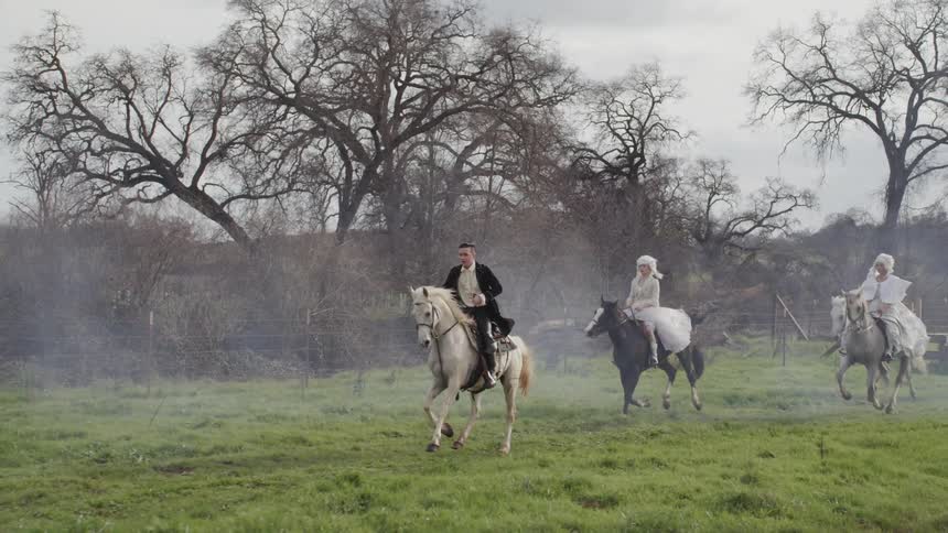 Four people in costumes are riding horses outside in the country in daylight