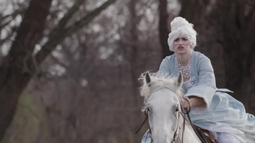 A woman in a large dress rides a horse