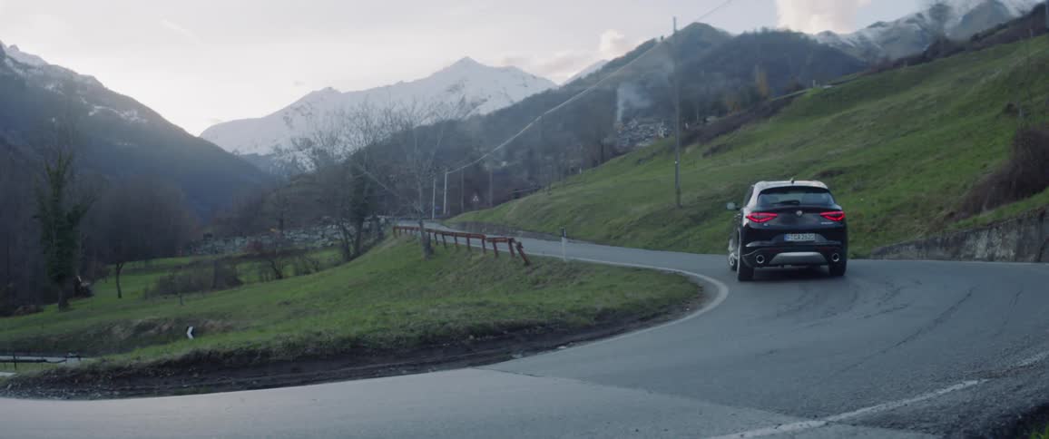 A car travels up a rural road on a cloudy day