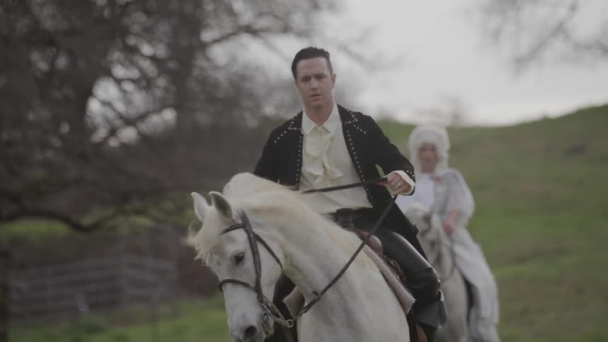 Man and woman ride white horses in a field on a cloudy day