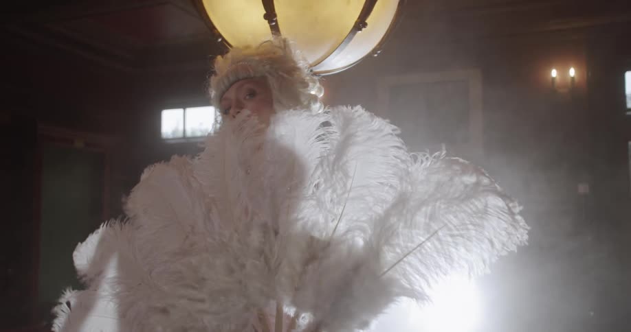 Woman in a wig holds a fan of large feathers