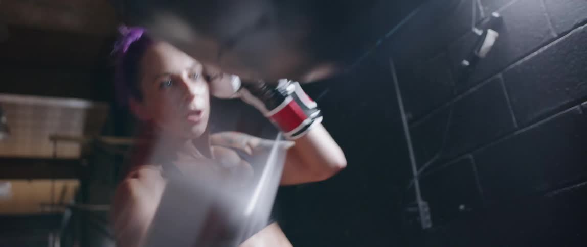 A woman is punching a medicine ball hanging from the ceiling