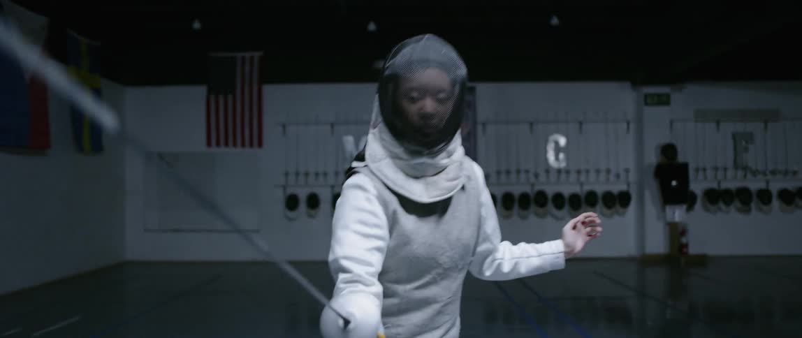 A woman in fencing gear and holding a sword practices her footwork