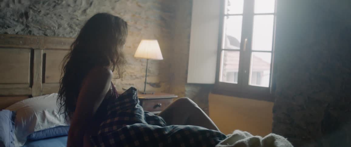 A woman pushes the covers off and sits up in bed looking out the window