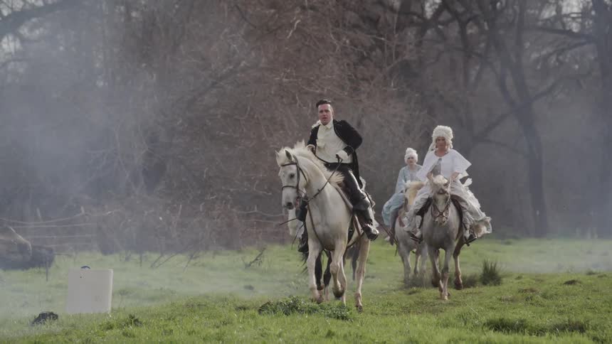 People in victorian era clothes ride horses on a foggy day