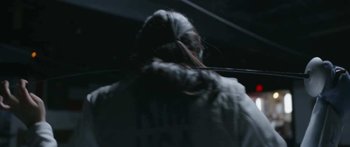 Person stands holding a fencing sword behind their shoulders