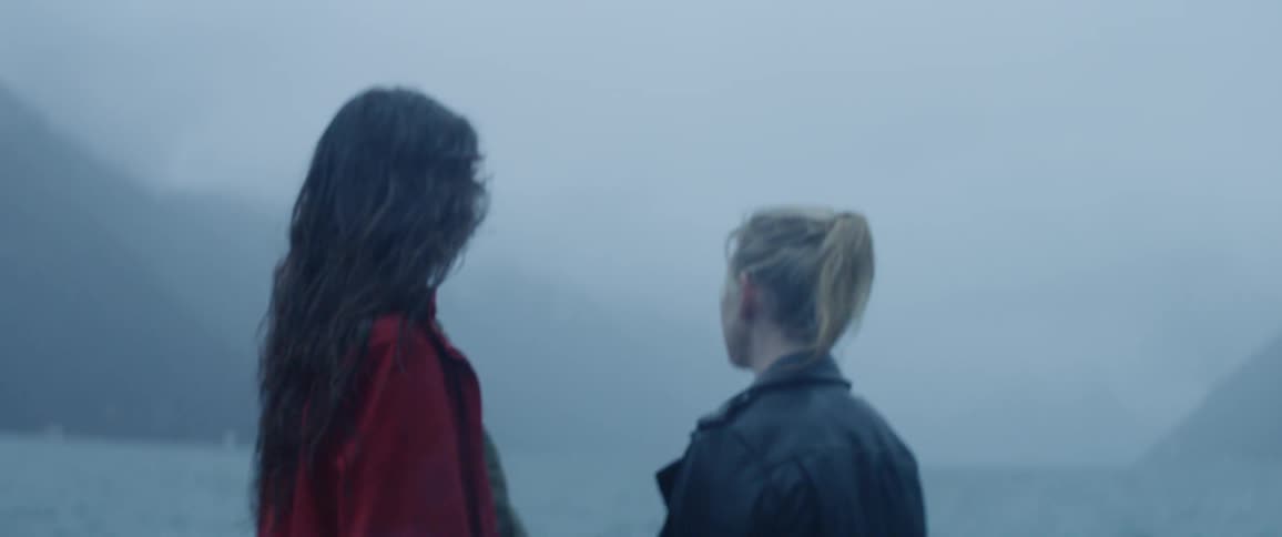 Two women stand next to a lake on a misty day
