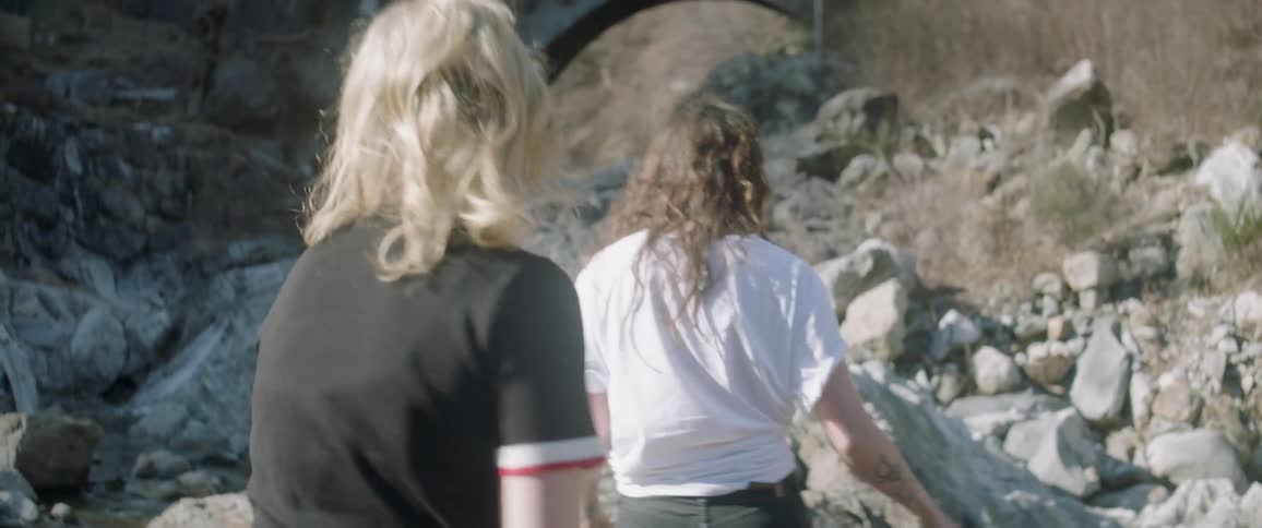 Two women walking through a creek near rocks
