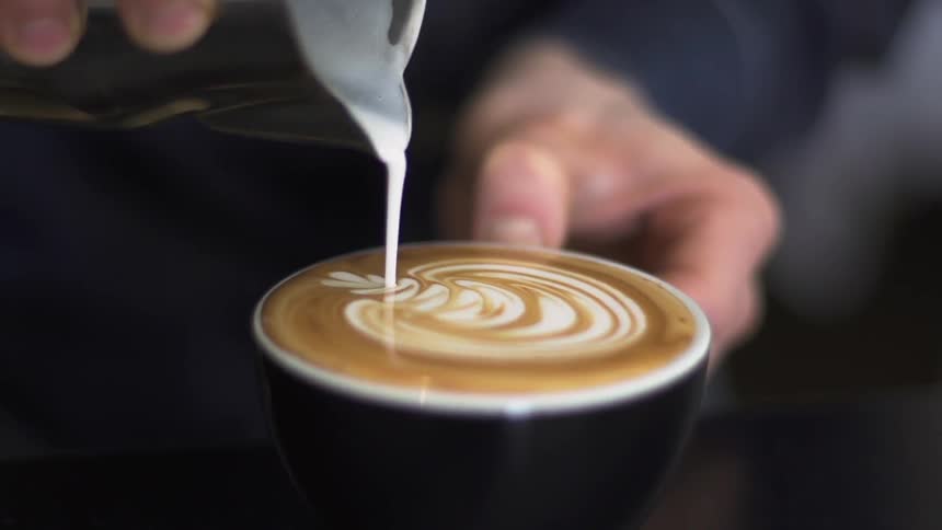 Person pours milk foam  into a cup of coffee
