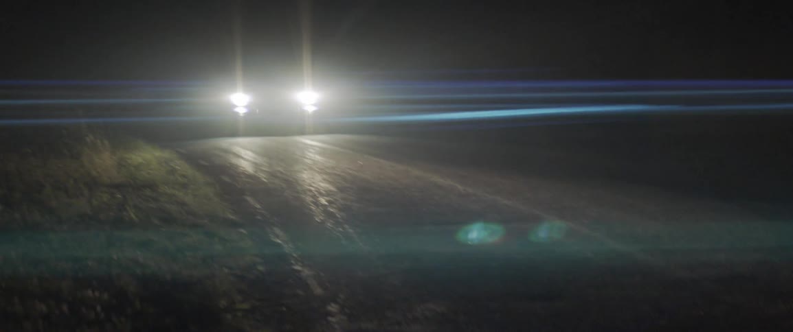 The car lights up the road as it drives at night
